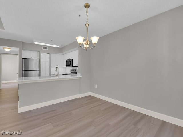 1180 Wildwood Lakes Blvd Unit 207, Naples, FL 34104 - kitchen with white cabinets, appliances with stainless steel finishes, a notable chandelier, and light wood-style floors