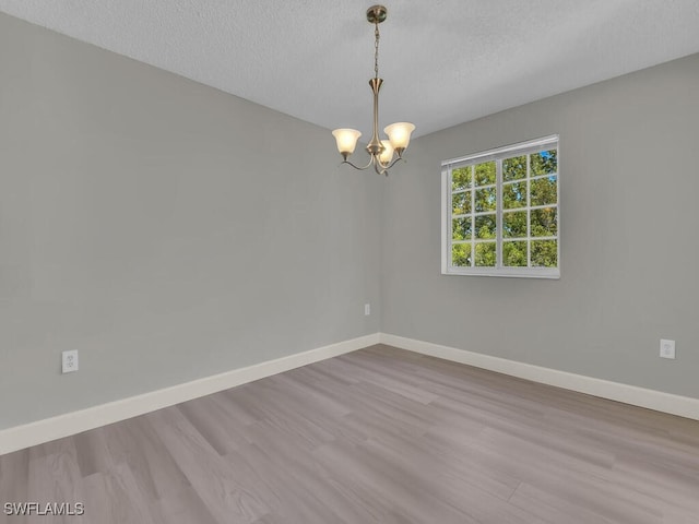 1180 Wildwood Lakes Blvd Unit 207, Naples, FL 34104 - empty room featuring a textured ceiling, baseboards, an inviting chandelier, and wood finished floors