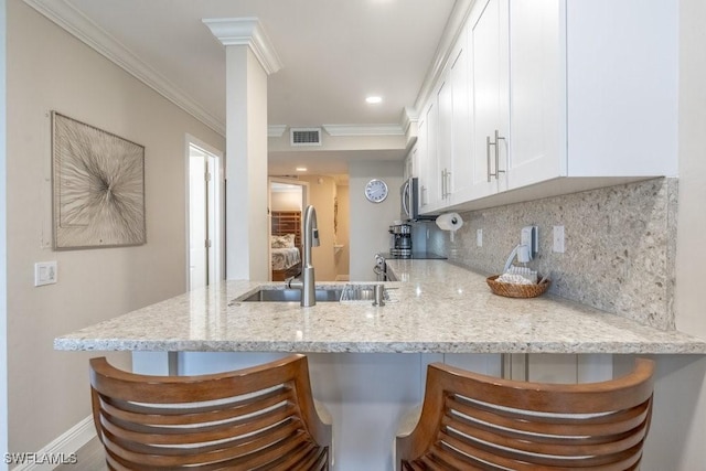 10 Tampa Pl Unit 401, Marco Island, FL 34145 - kitchen featuring a peninsula, ornamental molding, white cabinets, a sink, and backsplash