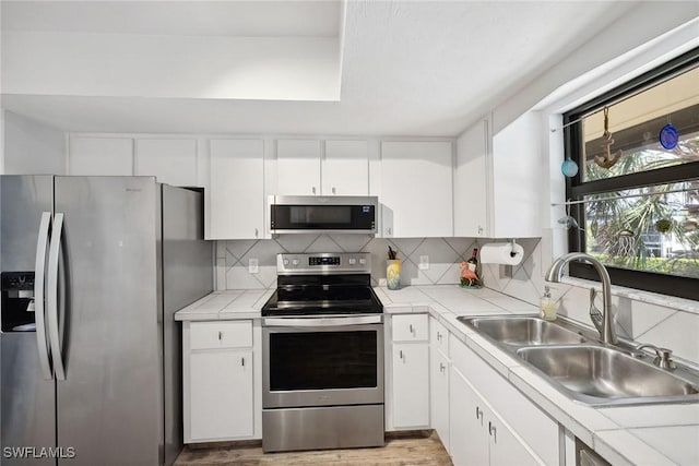 4967 Pepper Cir Unit 206, Naples, FL 34113 - kitchen featuring stainless steel appliances, a sink, white cabinets, backsplash, and light wood-style floors