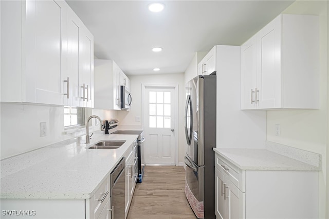 kitchen with white cabinetry, light wood-type flooring, stainless steel appliances, a sink, and light stone countertops