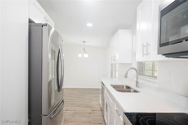 kitchen with a sink, a chandelier, light wood-type flooring, stainless steel appliances, and white cabinets
