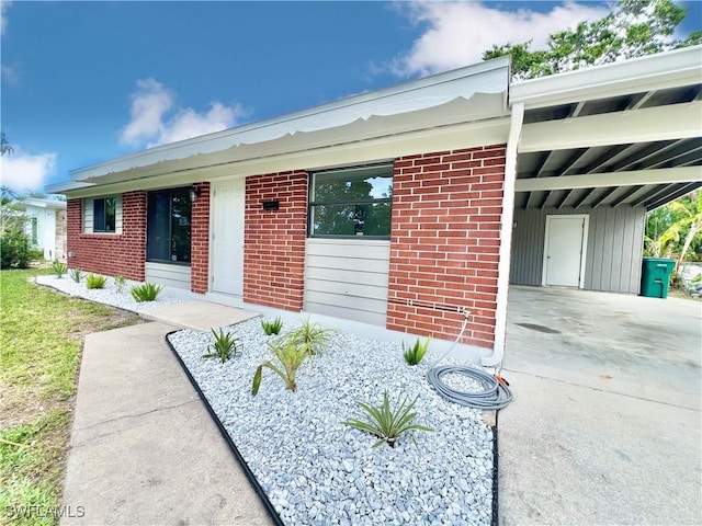 view of front of home with board and batten siding, an attached carport, brick siding, and concrete driveway