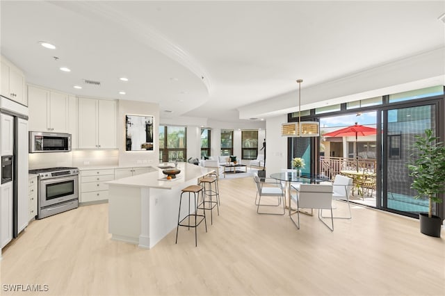 9123 Strada Pl Unit 7316, Naples, FL 34108 - kitchen featuring stainless steel appliances, light wood-style floors, a breakfast bar area, white cabinets, and decorative light fixtures