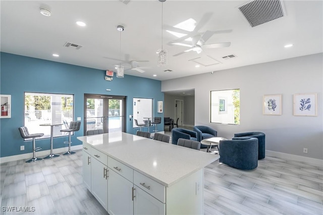 6235 Wilshire Pines Cir Unit 1408, Naples, FL 34109 - kitchen with ceiling fan, baseboards, light countertops, white cabinets, and a kitchen island