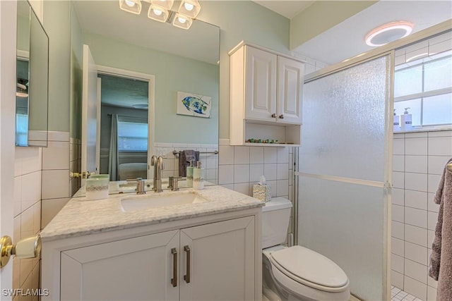 full bathroom with toilet, tile walls, a shower stall, vanity, and wainscoting