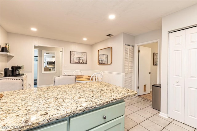 kitchen with visible vents, open shelves, green cabinetry, stainless steel microwave, and light tile patterned flooring