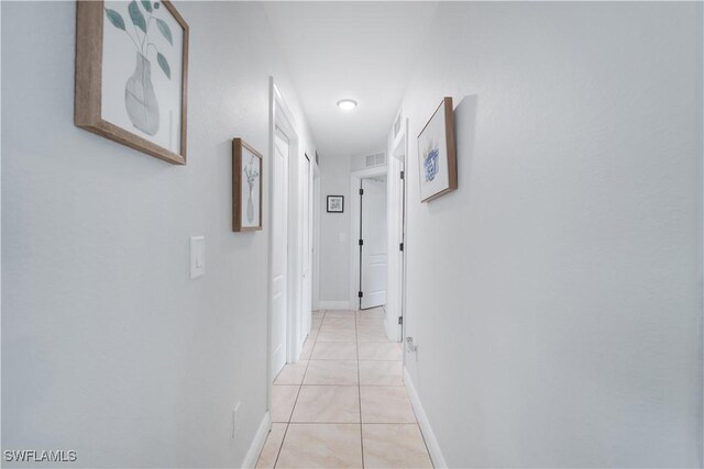 corridor with baseboards, visible vents, and light tile patterned floors