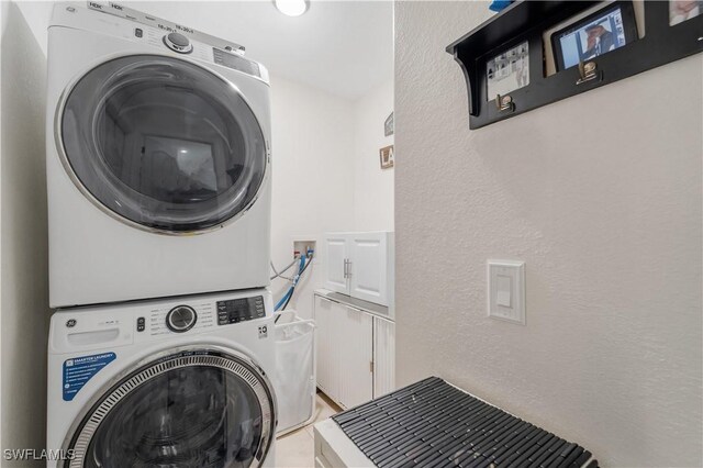 clothes washing area featuring a textured wall, stacked washer / drying machine, and laundry area