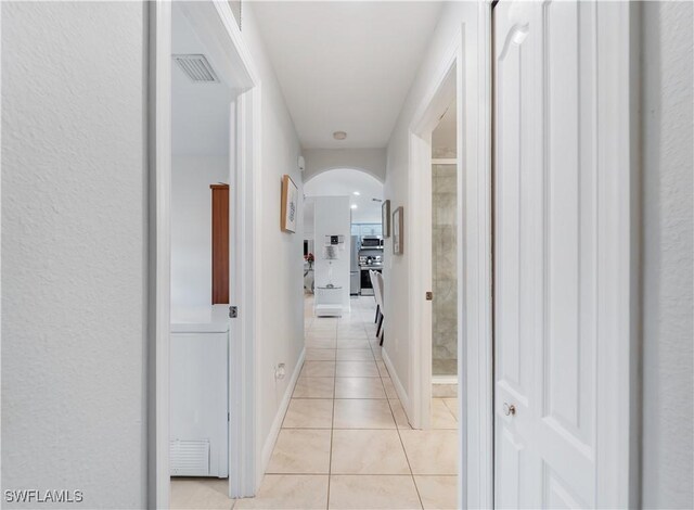 corridor featuring arched walkways, baseboards, visible vents, and light tile patterned flooring