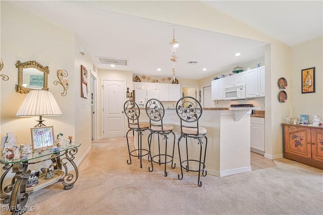 kitchen featuring a kitchen breakfast bar, light carpet, white cabinetry, and white appliances