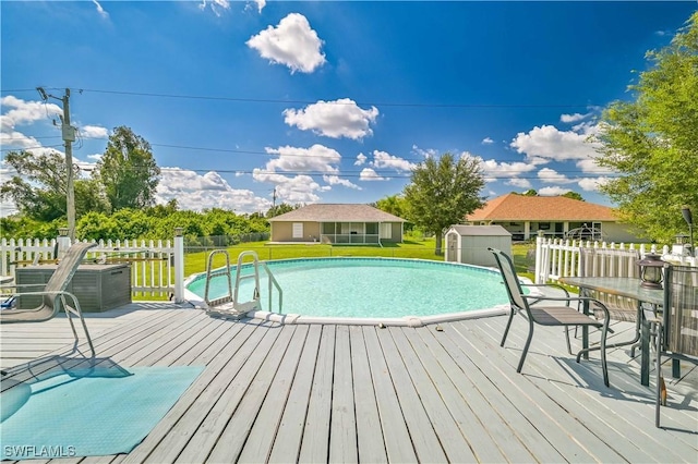 outdoor pool featuring an outbuilding, a shed, fence, a wooden deck, and a yard
