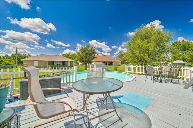 wooden deck with a fenced in pool, an outbuilding, fence, and outdoor dining space