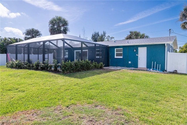 back of property with a yard, stucco siding, a lanai, and fence