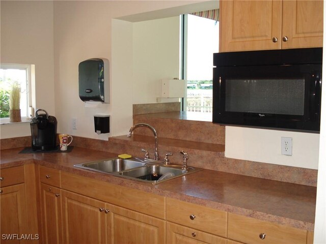 kitchen with light brown cabinetry, a sink, and black microwave