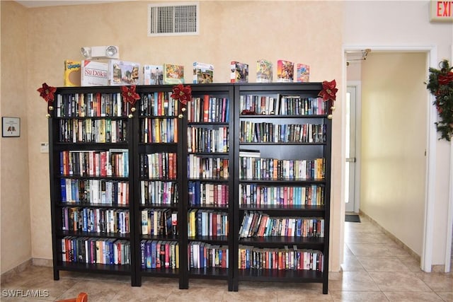 interior space featuring tile patterned floors, visible vents, bookshelves, and baseboards