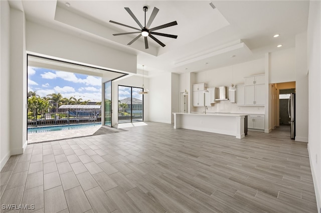 unfurnished living room with recessed lighting, a towering ceiling, a raised ceiling, light wood-type flooring, and ceiling fan
