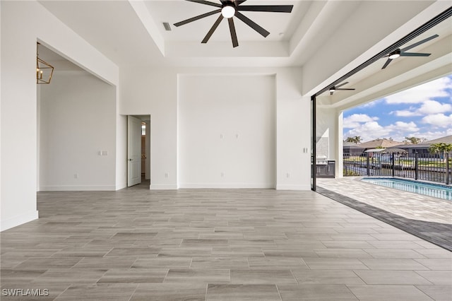 empty room featuring a tray ceiling, a ceiling fan, and a towering ceiling