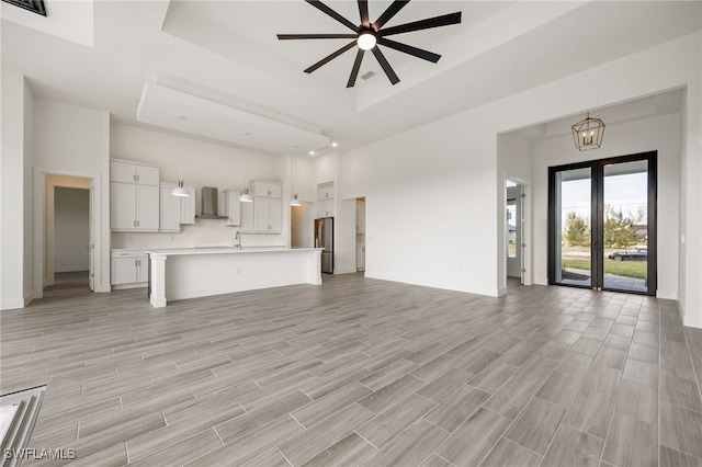 unfurnished living room with baseboards, a high ceiling, a ceiling fan, and light wood-style flooring