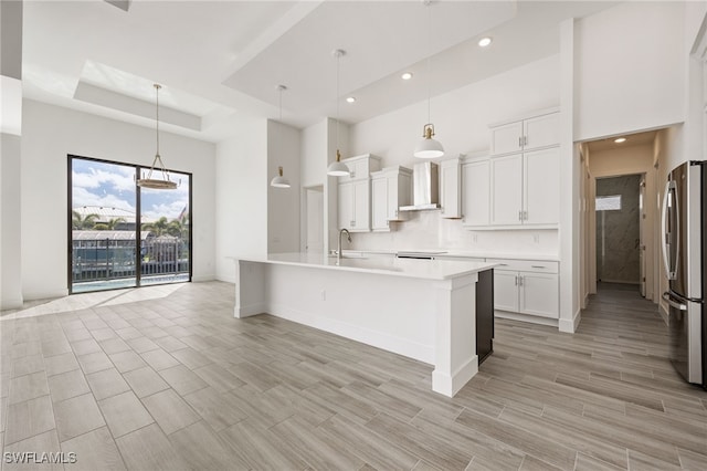 kitchen featuring a sink, freestanding refrigerator, a towering ceiling, wall chimney exhaust hood, and recessed lighting