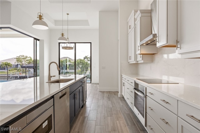 kitchen featuring a sink, backsplash, appliances with stainless steel finishes, a raised ceiling, and hanging light fixtures