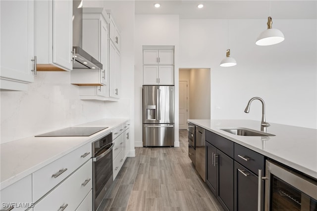 kitchen with wall chimney exhaust hood, stainless steel appliances, wine cooler, a sink, and white cabinetry