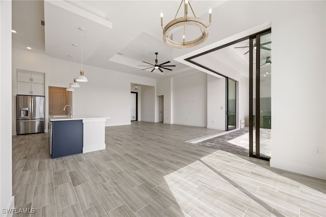 unfurnished living room with wood tiled floor, a raised ceiling, a sink, baseboards, and ceiling fan with notable chandelier