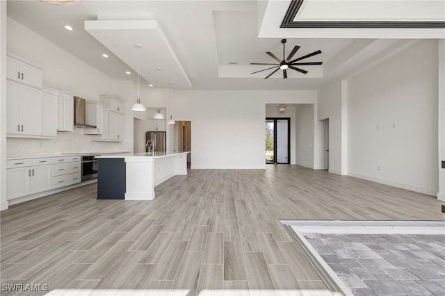kitchen featuring open floor plan, wall chimney exhaust hood, appliances with stainless steel finishes, and a raised ceiling