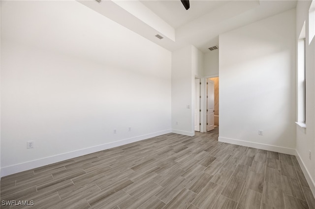 empty room featuring light wood-type flooring, visible vents, baseboards, and a high ceiling