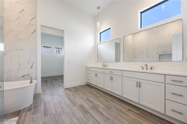 full bathroom featuring double vanity, wood finished floors, a sink, baseboards, and a freestanding tub