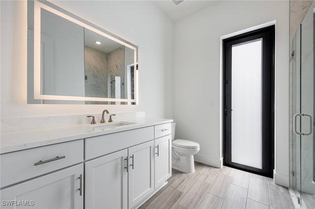 bathroom with toilet, vanity, a marble finish shower, and baseboards