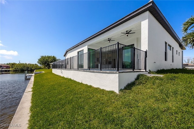 view of side of home with stucco siding, a water view, a yard, and ceiling fan