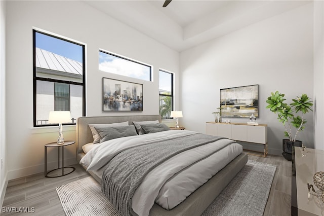 bedroom featuring a high ceiling, light wood finished floors, baseboards, and a ceiling fan