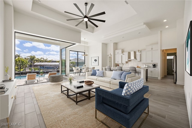 living area featuring a high ceiling, a ceiling fan, a tray ceiling, and recessed lighting
