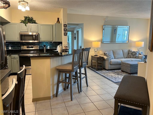 15585 Ocean Walk Cir Unit 216, Fort Myers, FL 33908 - kitchen featuring appliances with stainless steel finishes, dark countertops, light tile patterned floors, open floor plan, and tasteful backsplash