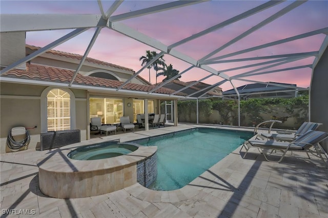 pool at dusk with a lanai, a pool with connected hot tub, and a patio area