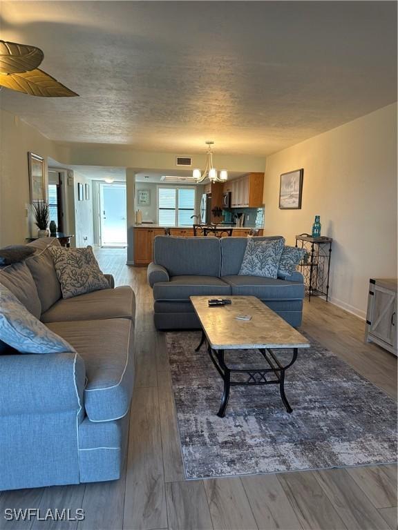 4244 SE 20th Pl Unit 218, Cape Coral, FL 33904 - living room featuring baseboards, a chandelier, a textured ceiling, light wood-style floors, and visible vents