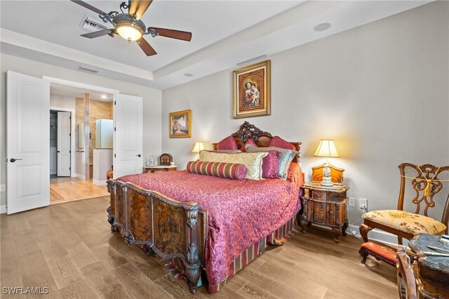 9435 Night Heron Ln, Naples, FL 34120 - bedroom featuring a tray ceiling, a ceiling fan, freestanding refrigerator, wood finished floors, and visible vents