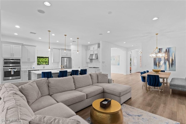living area with a chandelier, recessed lighting, arched walkways, and light wood-style flooring