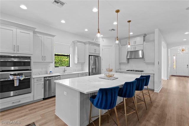 kitchen featuring a sink, under cabinet range hood, a center island, visible vents, and appliances with stainless steel finishes