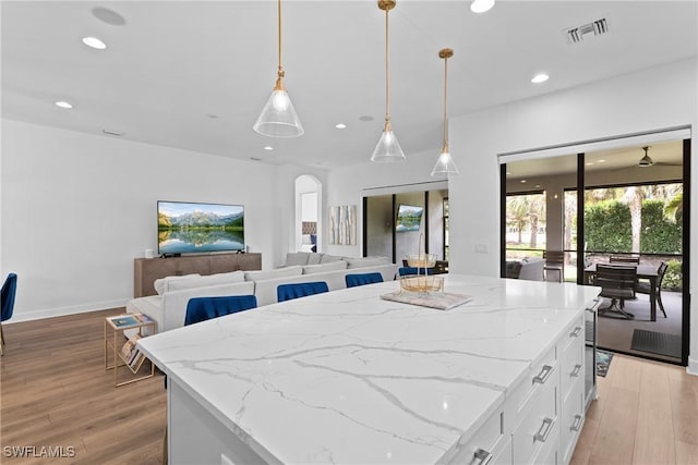 9336 Montelanico Loop, Naples, FL 34119 - kitchen with arched walkways, light wood-type flooring, recessed lighting, white cabinetry, and light stone countertops