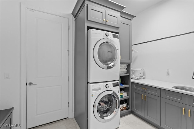 washroom featuring light tile patterned floors, a sink, cabinet space, and stacked washing maching and dryer