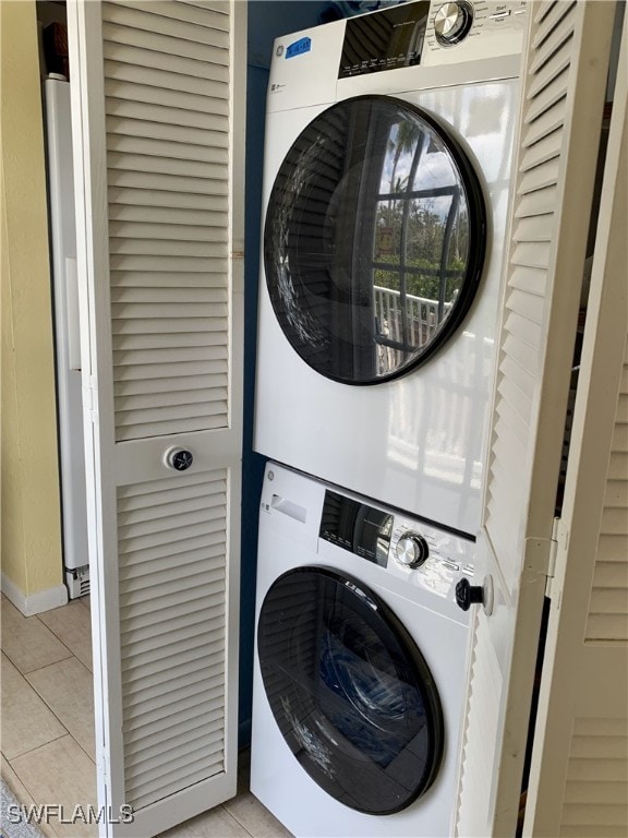 clothes washing area with baseboards, light tile patterned floors, laundry area, and stacked washer / dryer