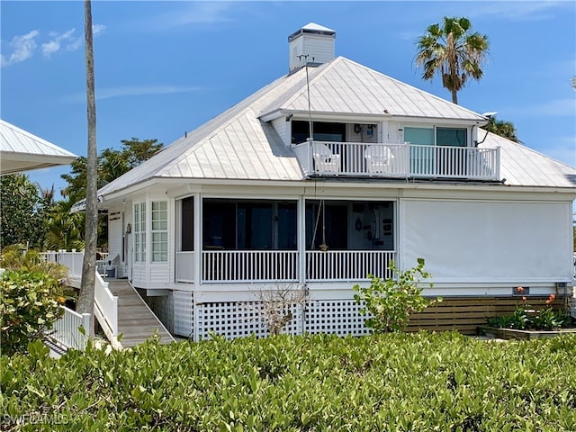 view of front of house featuring a standing seam roof, a chimney, a sunroom, stairway, and a balcony