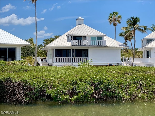 back of property with a standing seam roof, a water view, metal roof, and a balcony