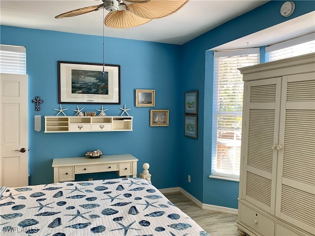 bedroom with baseboards, ceiling fan, multiple windows, and wood finished floors