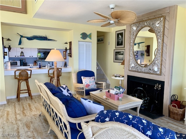 living room with a ceiling fan, wood finished floors, and a large fireplace