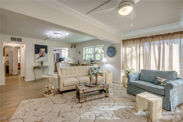 living room with baseboards, ornamental molding, light wood-style flooring, visible vents, and ceiling fan