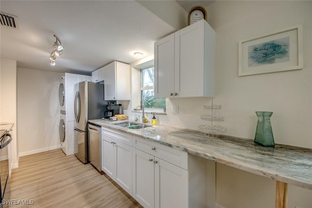 kitchen featuring stacked washer and clothes dryer, white cabinetry, visible vents, dishwasher, and a sink