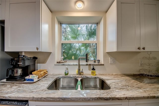 kitchen featuring white cabinets, light stone countertops, dishwasher, and a sink